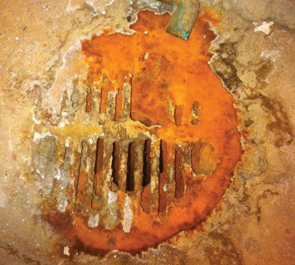 Severe floor drain corrosion caused by untreated acidic condensate from high-efficiency heating appliances.