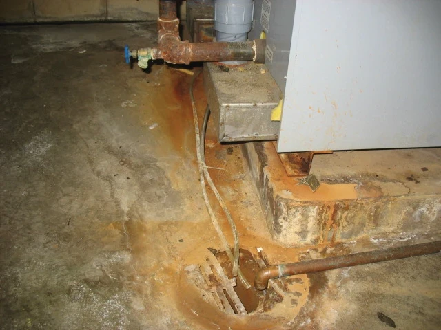 Condensate corrosion damage to concrete floor and drain caused by untreated furnace condensate